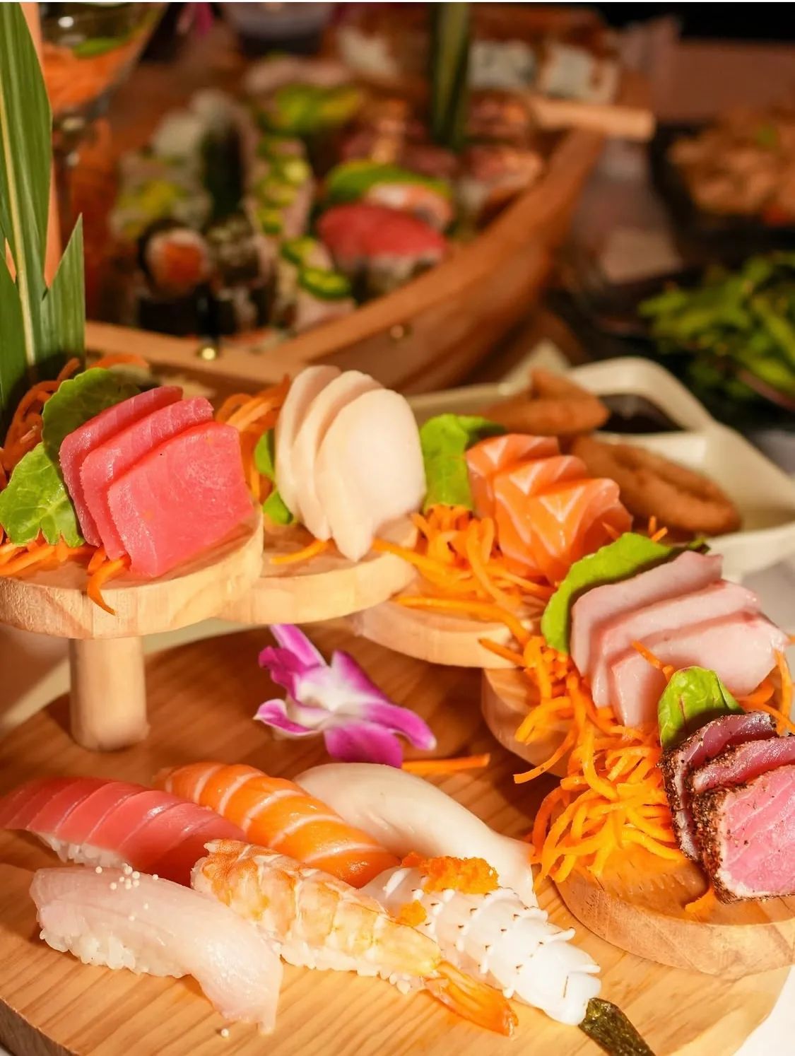 Sashimi on tiered wooden stands above a board of nigiri, with an orchid in the middle