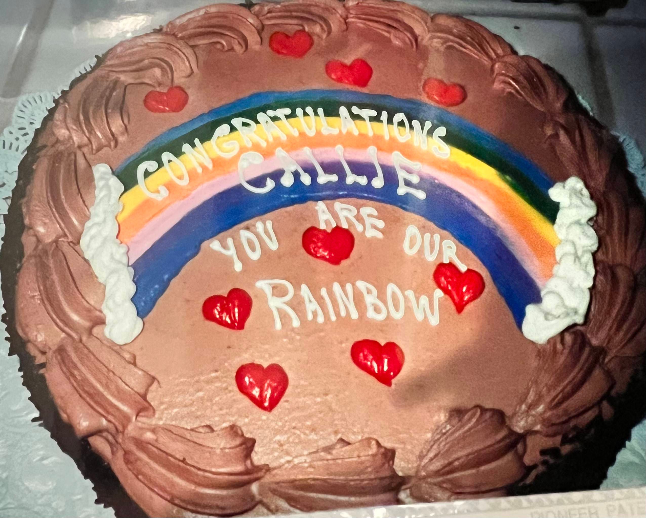 a cake with chocolate frosting, a rainbow made of frosting with red frosting hearts and frosting text which reads "congratulations Callie you are a rainbow"