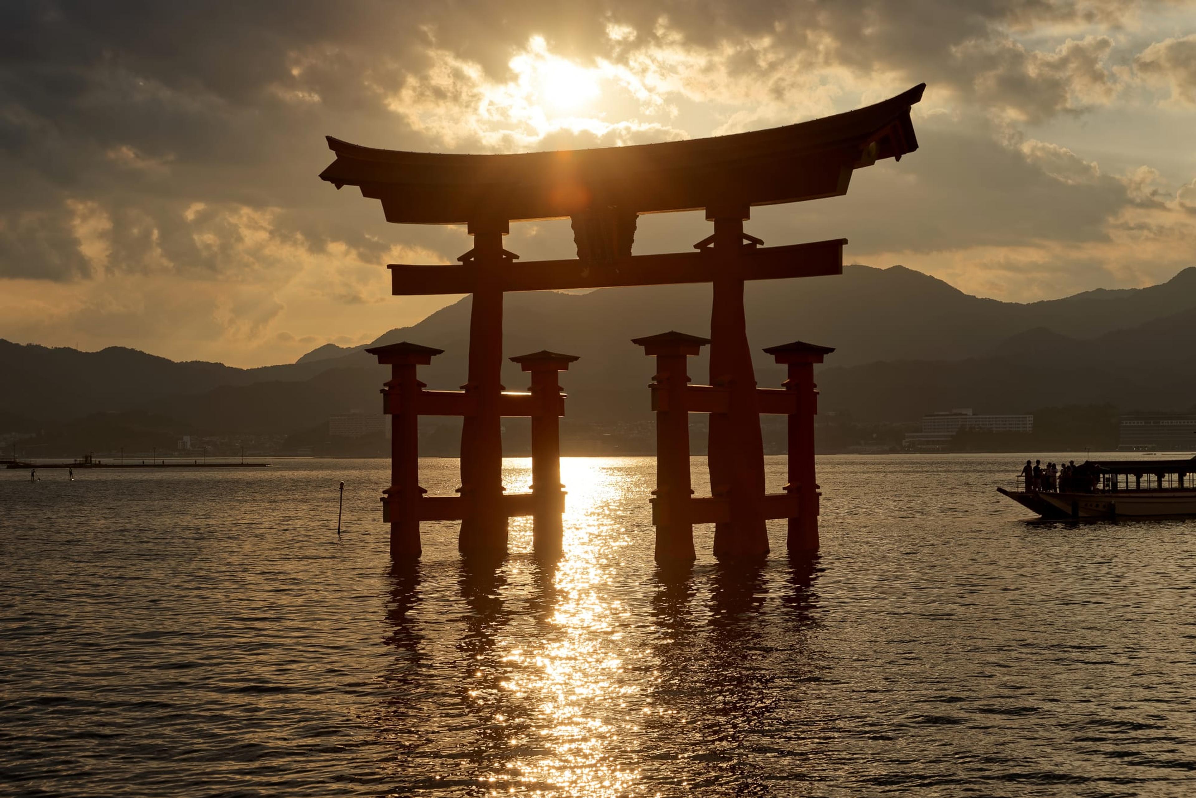 The floating torii gate of Itsukushima Shrine at sunset, seen across the water from Miyajima