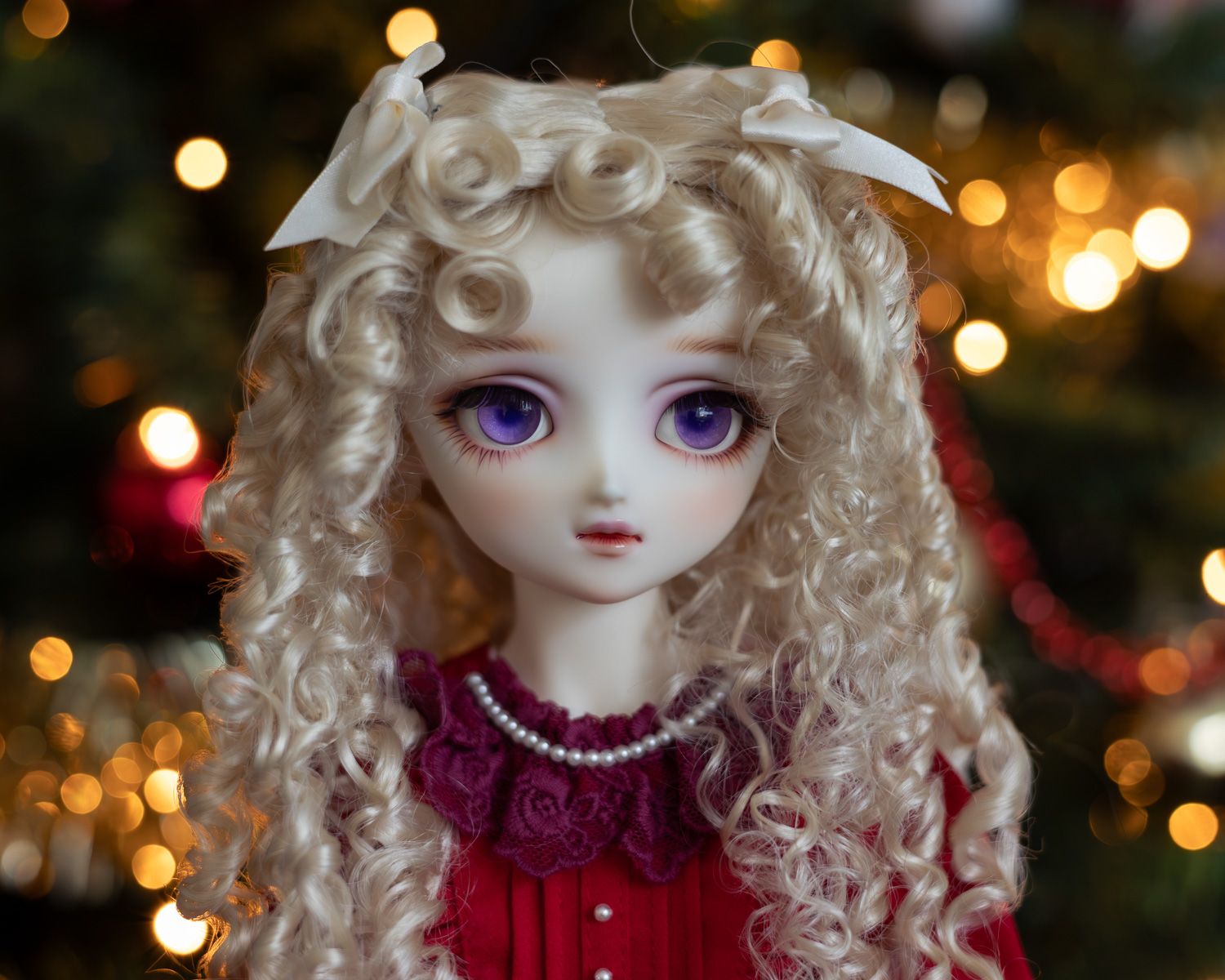 Portrait of a female ball-jointed doll with long blonde hair in ringlets and big purple eyes, wearing a red dress. She is looking away from the camera, to the side.