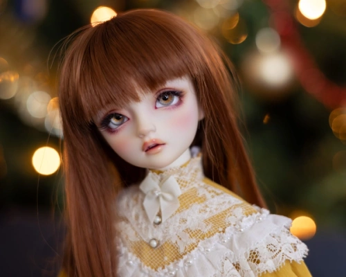 Portrait of a female ball-jointed doll with long auburn hair, wearing a high-necked yellow and white dress. She is in front of an out-of-focus Christmas tree.