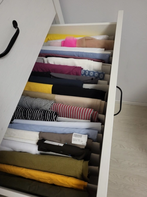 An open drawer filled with many different fabrics, neatly folded.