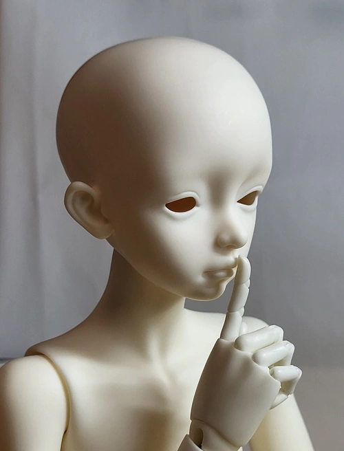 Three-quarter portrait view of a male ball-jointed doll with a finger to its lips. The visible hand has jointed fingers.