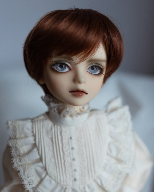 Portrait photo of a male resin ball-jointed doll (MSD Hewitt). He has a childlike face, pale blue-grey eyes, a red-brown wig, and wears a ruffled white shirt with pintucks and lace.