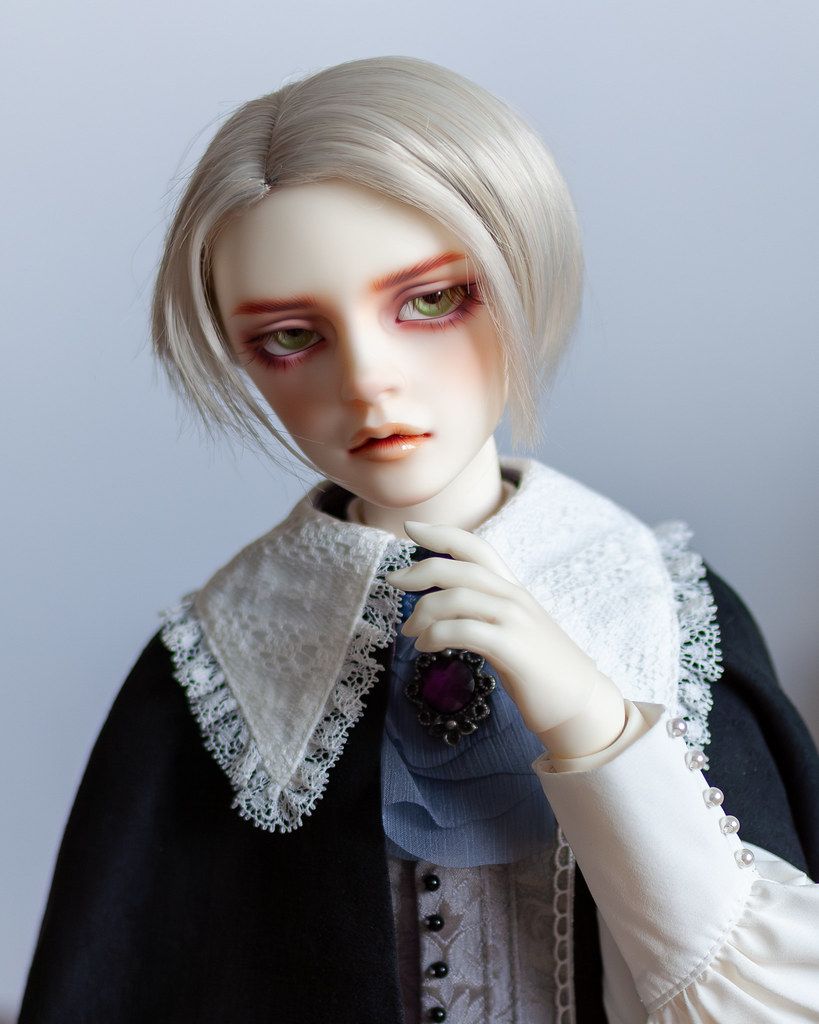 Male resin ball-jointed doll with short silver hair, pale green eyes and a sulky face, wearing a cloak with a lace collar.