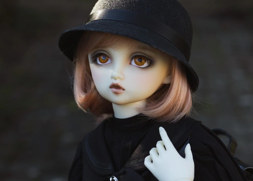 Portrait photo of a ball-jointed resin doll. She is outside in a garden with grey tiles behind her, wearing a black old-fashioned school uniform and a cloche hat. She carries a black school bag on her back. Her resin is pale white, her eyes are orange and her bobbed hair is peach.