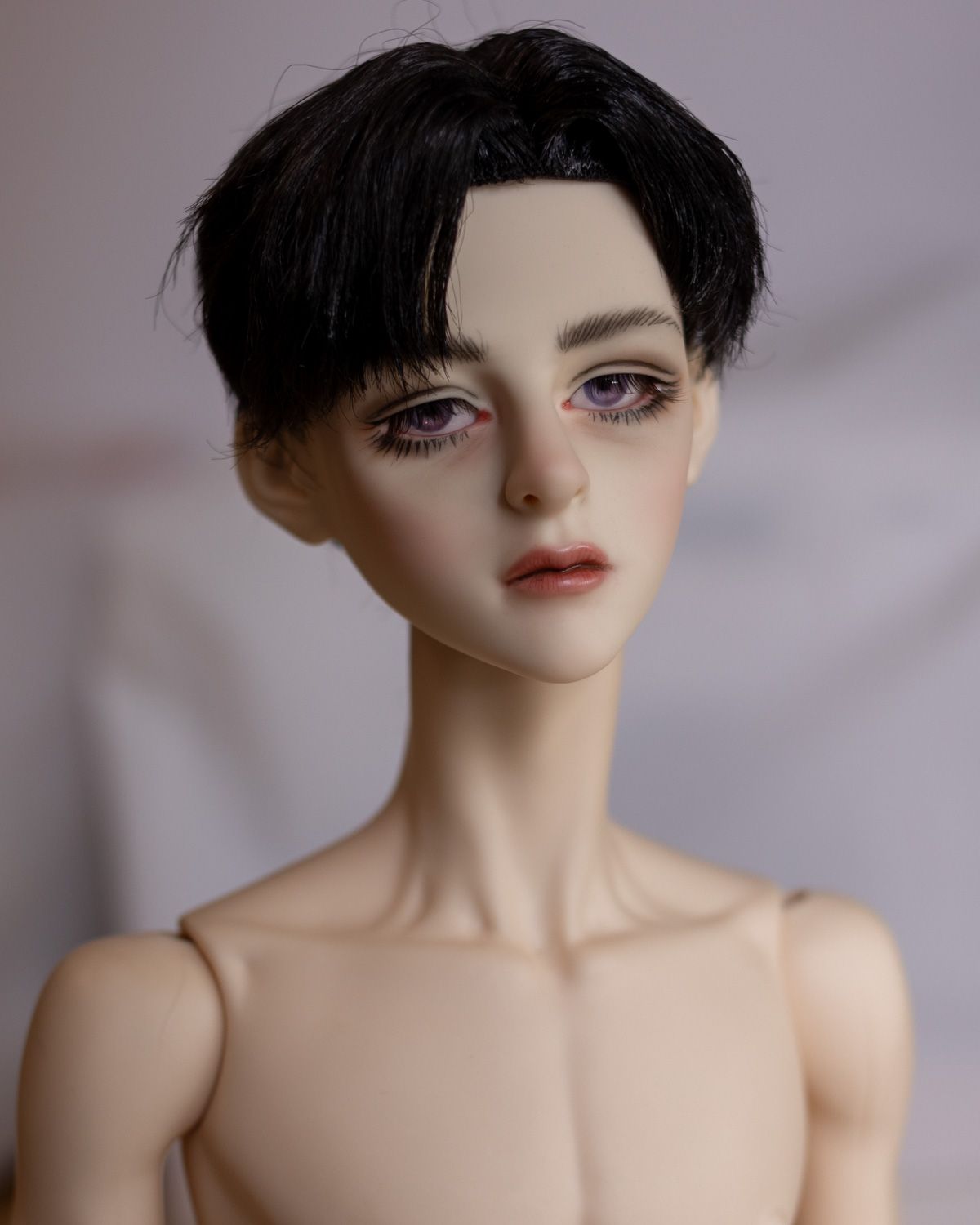 Portrait photo of a male ball-jointed doll with short black hair with 90s-style bangs, thick spidery lashes and a very amateurish faceup.