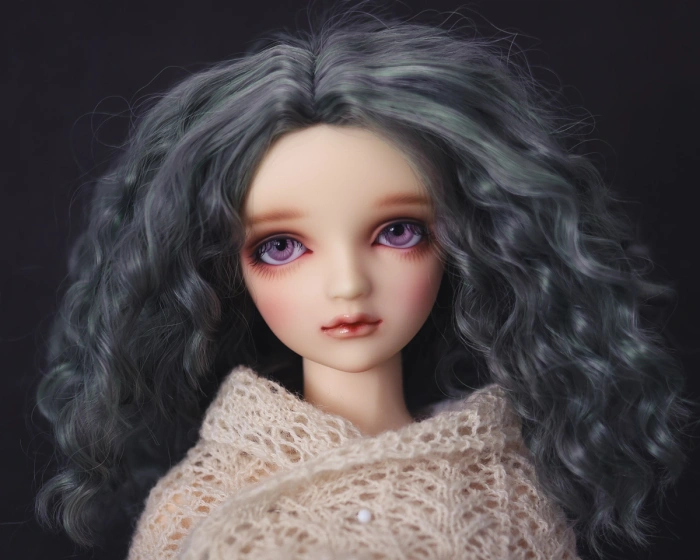 Portrait of a female ball-jointed resin doll with dark green hair and pink eyes, wearing a cream knitted lace shawl.