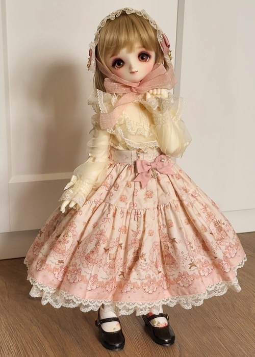 A full-length view of a ball-jointed doll with large eyes, wearing a frilly blouse, lolita-style headdress and a big floofy skirt with a cute rabbit and flower print.