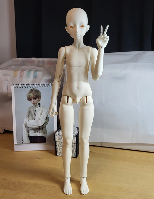Male ball-jointed doll standing on a table with one hand raised in a V-pose.