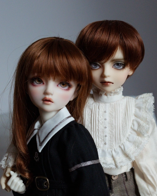 Photo of two resin ball-jointed dolls, a girl (Hazel) and a slightly taller boy (Hewitt), standing close together. They both have red-brown hair. The girl wears a black school uniform with a white collar, and the boy wears a very frilly white shirt with lace.