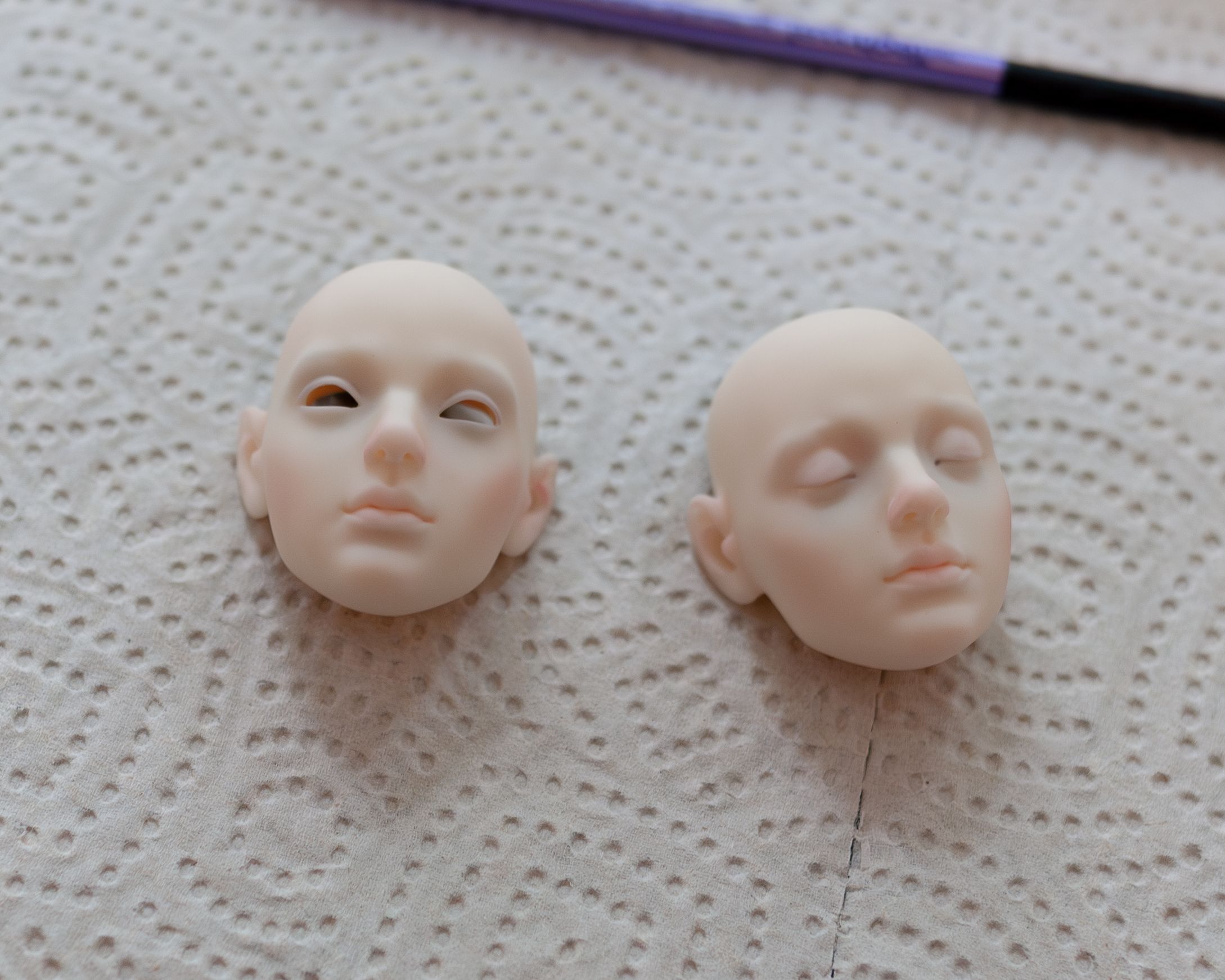 Two faceplates for a resin ball-jointed doll. One has open eyes, the other closed eyes. They are partially painted.