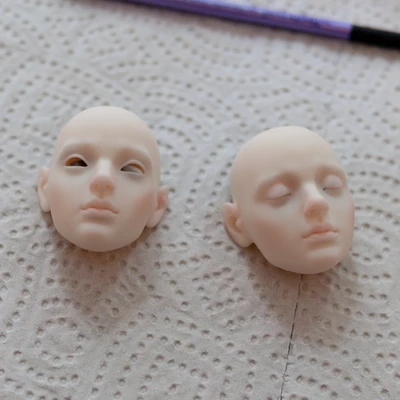 Two faceplates for a resin ball-jointed doll. One has open eyes, the other closed eyes. They are partially painted.