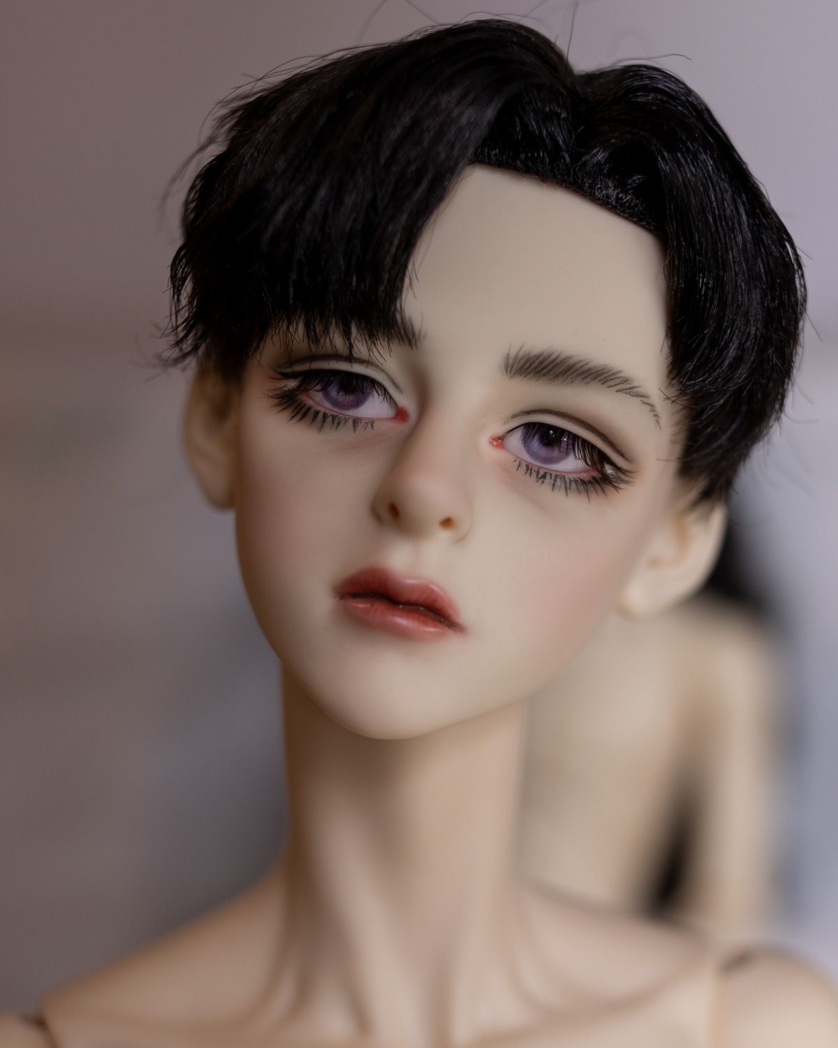 Portrait photo of a male ball-jointed doll with short black hair with 90s-style bangs, thick spidery lashes and a very amateurish faceup.