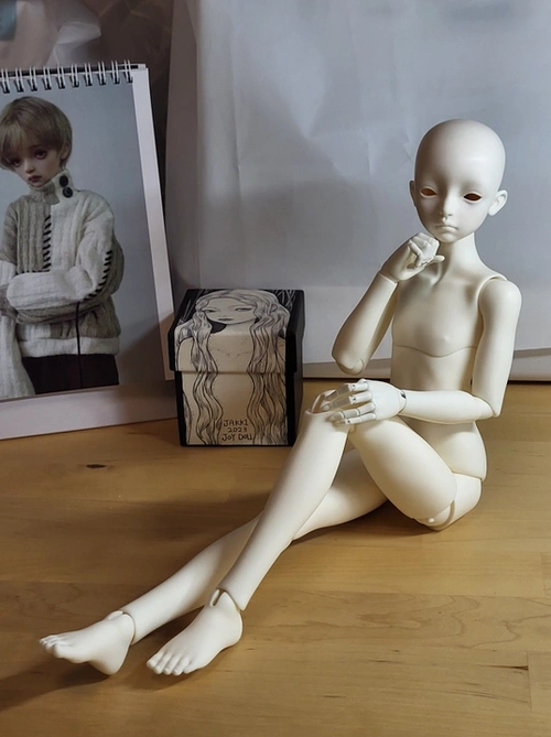 Male ball-jointed doll sitting on a table with one knee raised, one hand in a loose fist under its chin.
