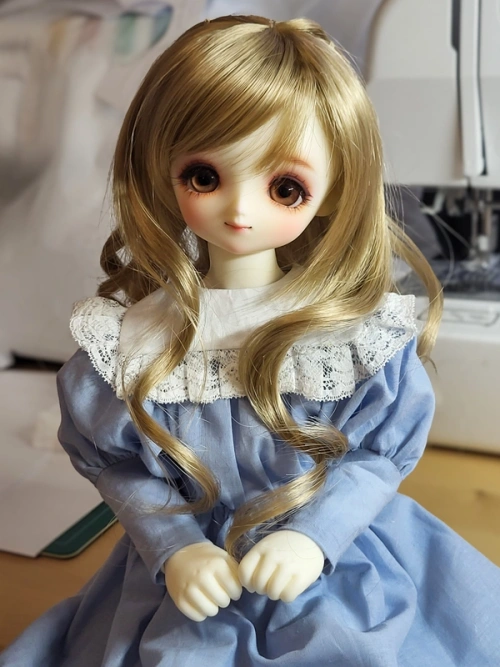 A big-eyed ball-jointed doll wearing a light blue dress with puffy sleeves and a lace-edged collar.