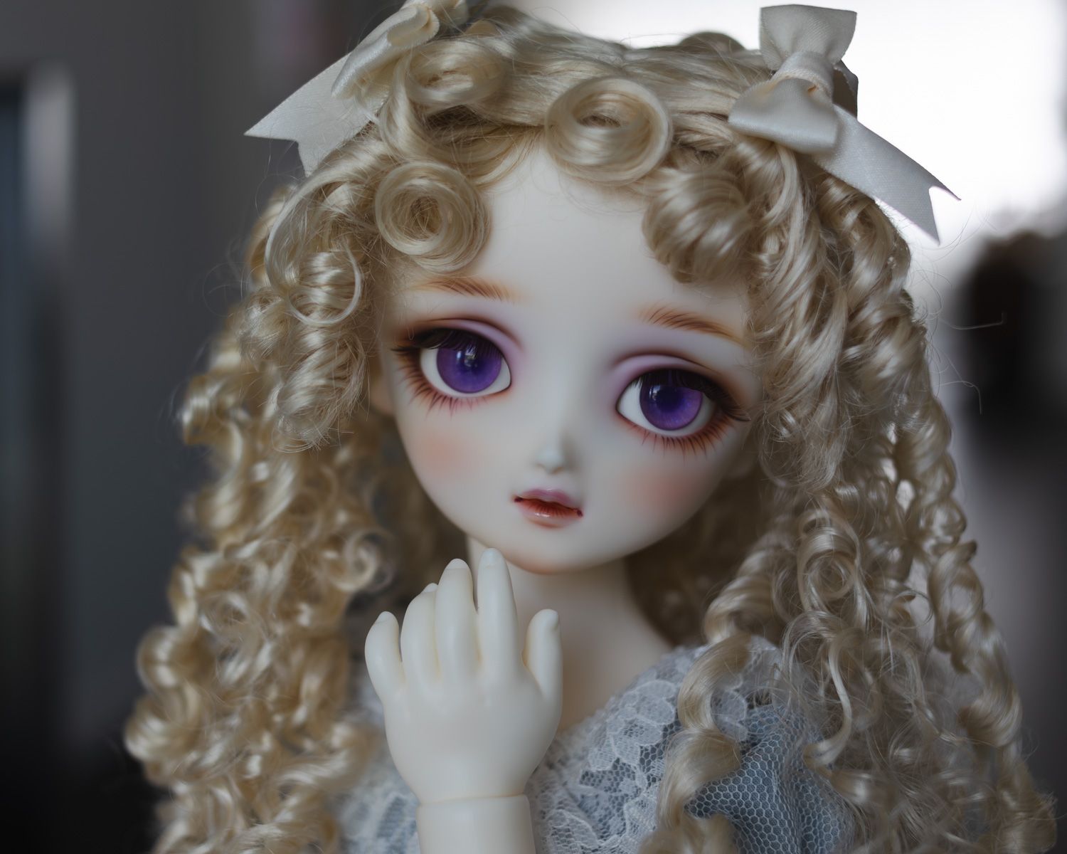 Female ball-jointed resin doll with pale skin, long blonde hair in ringlets, and big wide purple eyes.