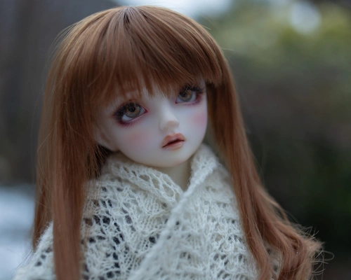 Portrait photo of a female ball-jointed doll with auburn hair, standing outside in the snow and wearing a cream knitted shawl.