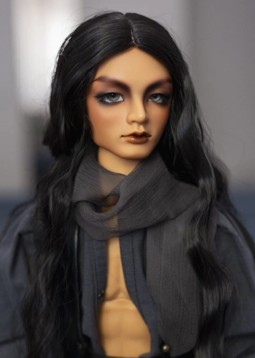 Male ball-jointed doll with tan skin and strongly-marked eyebrows, with grey eyes and long black hair. He wears an open grey shirt with a gauzy grey scarf around his neck.