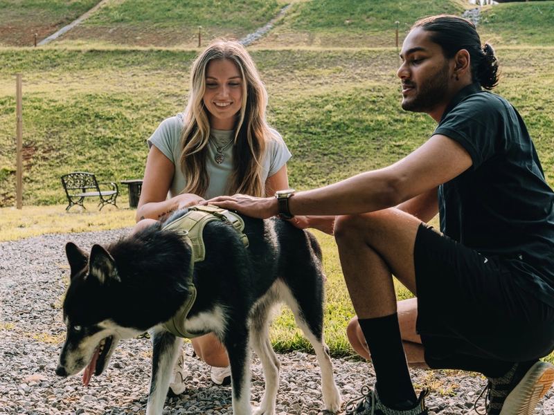 A couple crouched together petting their dog beside the trail at Sojourn Lodging