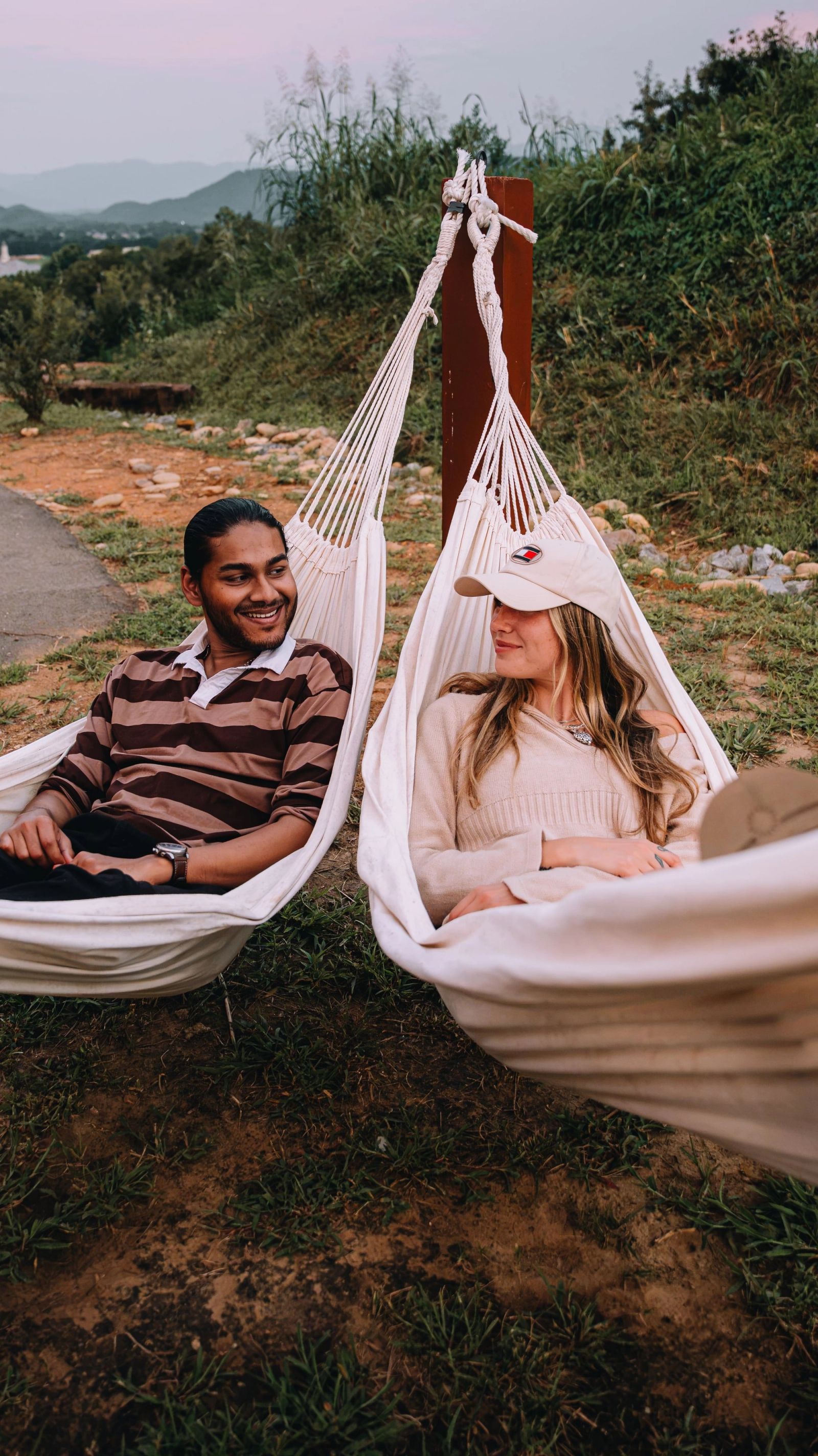 A couple lying in hammocks at Sojourn Lodging with the Smoky Mountains on the horizon at dusk