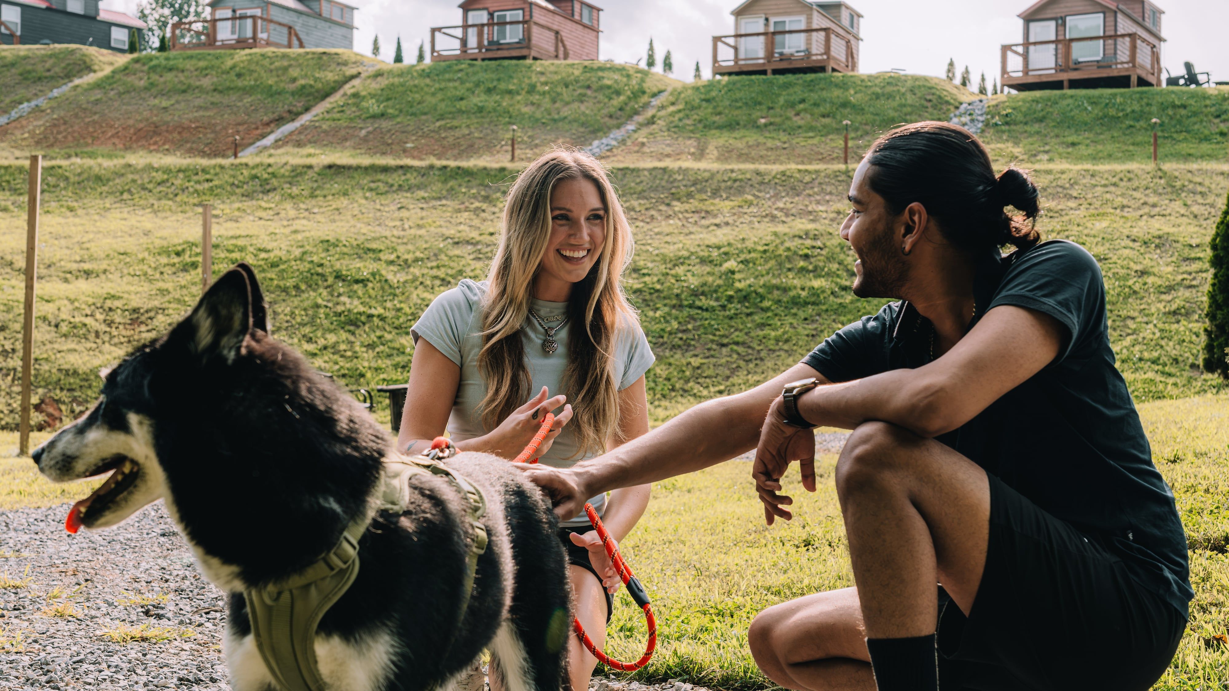 A couple with their dog on the path, tiny homes lining the hillside behind