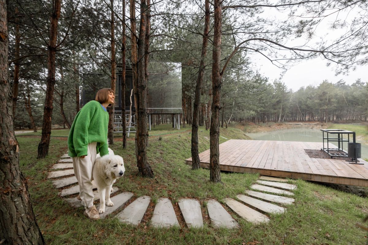 Woman and a dog in front of a mirror cabin and adjacent walkway.