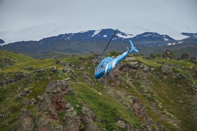 Helicopter flying over green mountain tops.