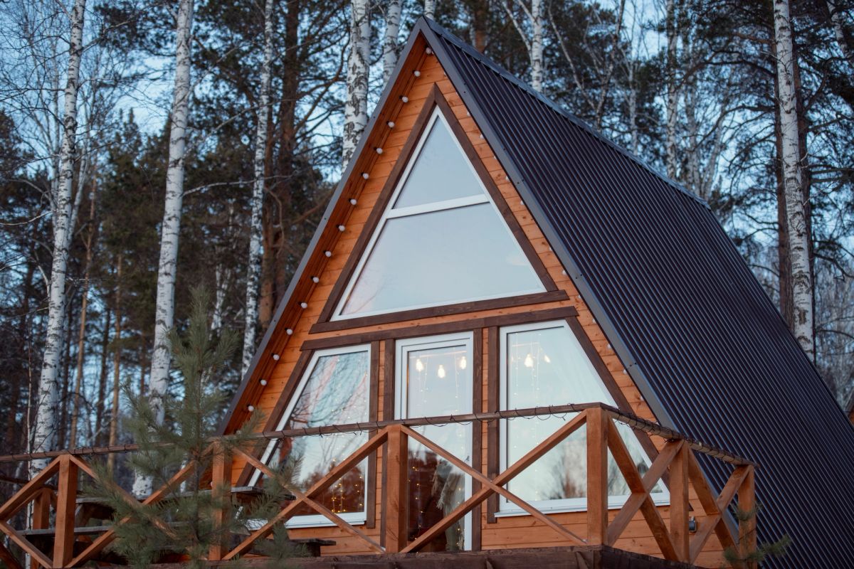 Top of an a-frame wooden cabin with large windows and a balcony.