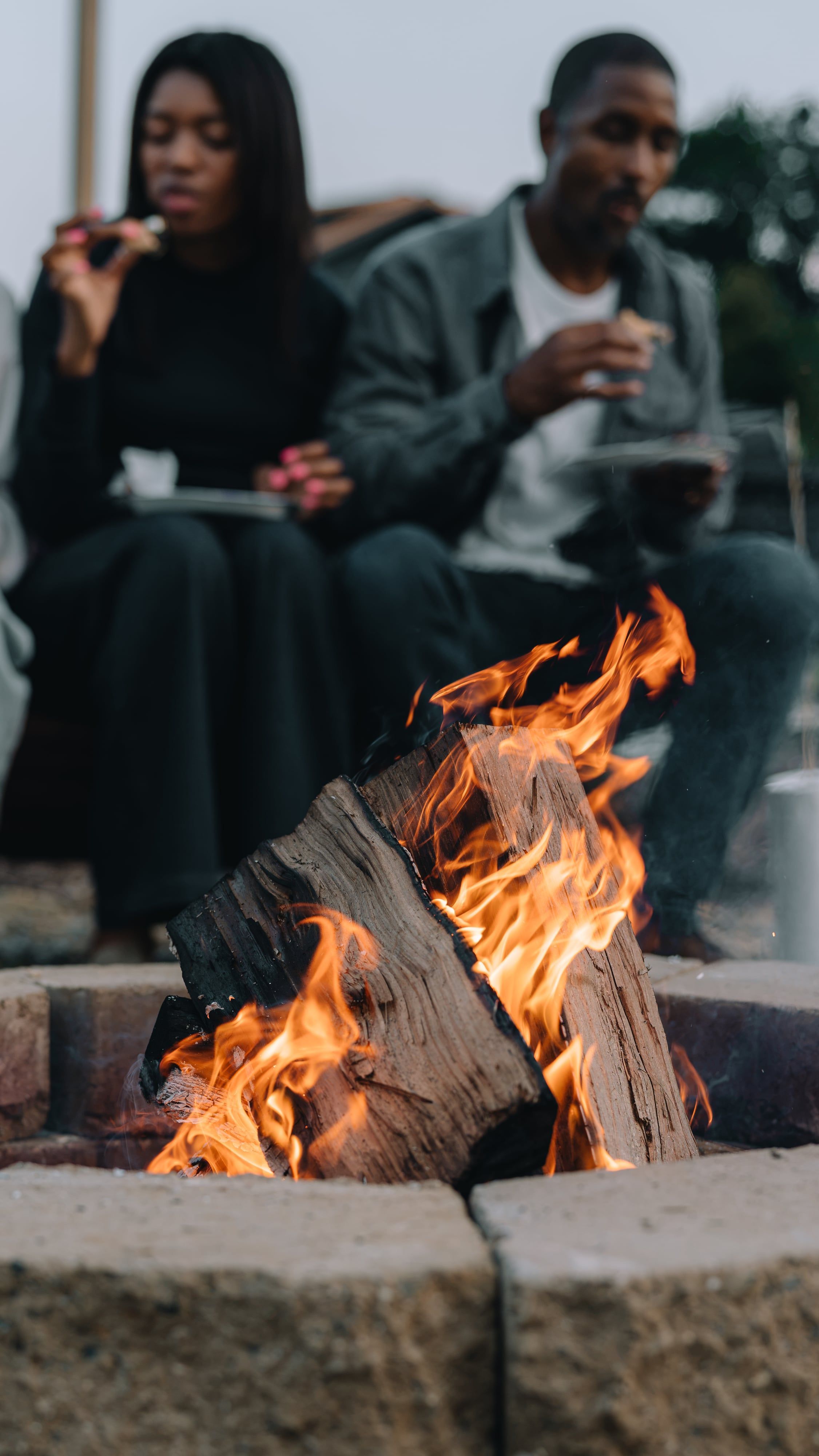 A couple eating s'mores seen behind the firepit flames at Sojourn Lodging
