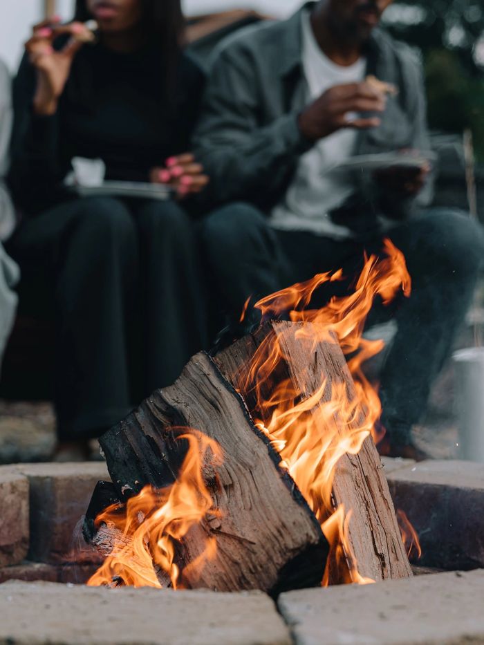 A couple eating s'mores seen behind the firepit flames at Sojourn Lodging