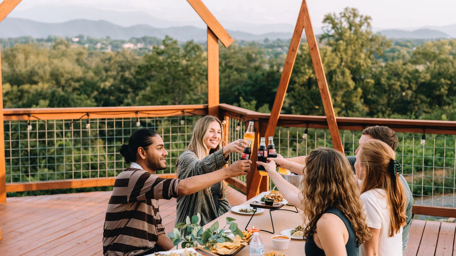 Friends reaching in to toast around the Observation Deck table with the Smoky Mountains behind