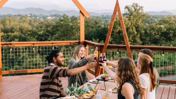 Friends reaching in to toast around the Observation Deck table with the Smoky Mountains behind