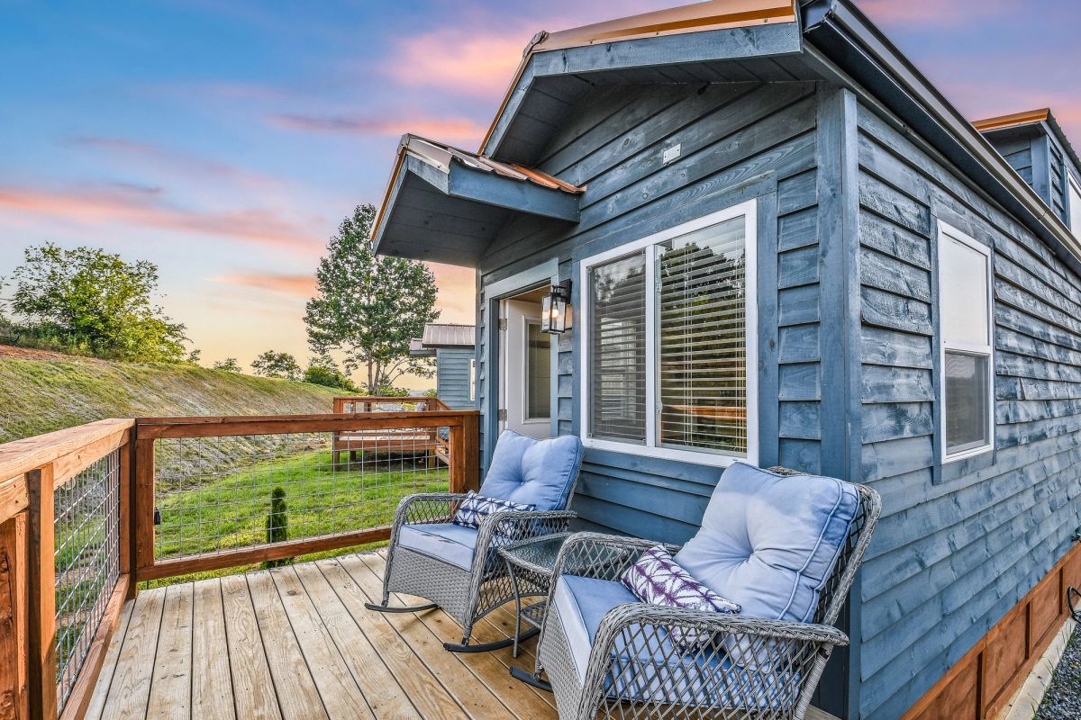 Sojourn tiny home exterior with private deck and wicker chairs under a vibrant sunset sky