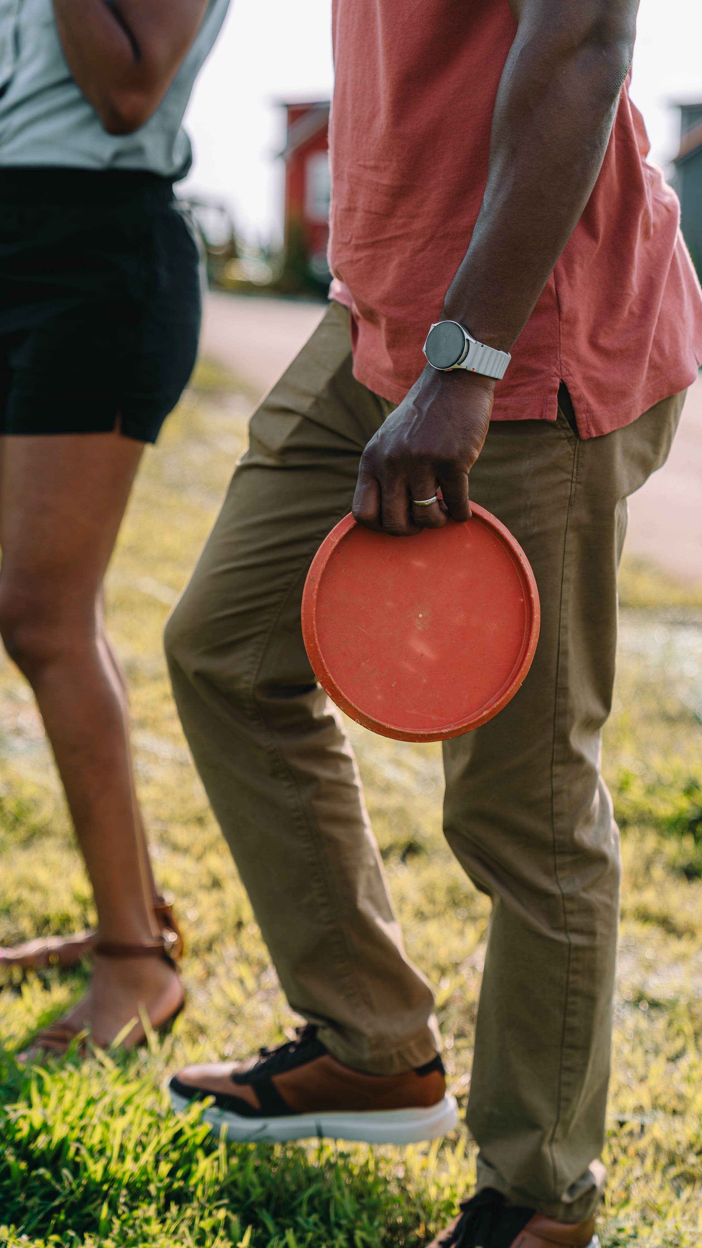 Detail of a guest holding a red disc golf disc at their side on the lawn at Sojourn Lodging