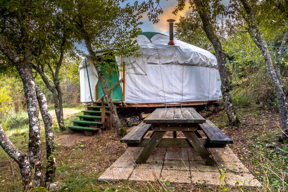 White canvas yurt in between trees with a picnic table to its right.
