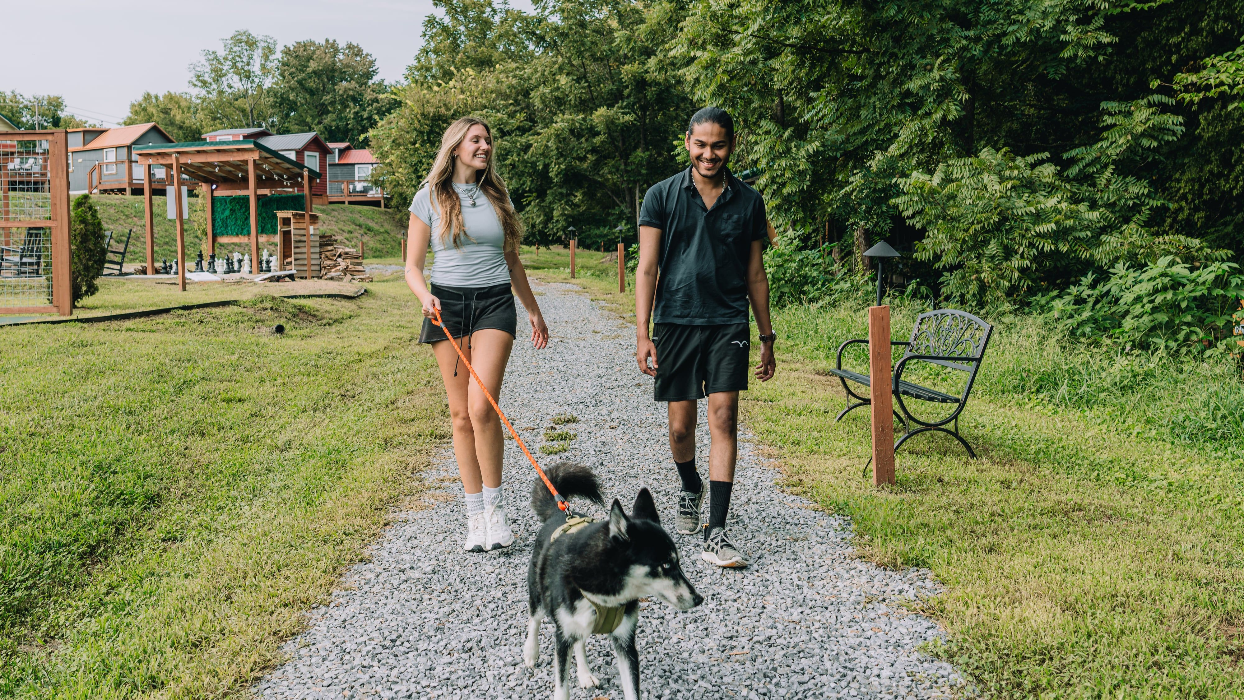 A couple walking their dog down the trail past a bench at Sojourn Lodging