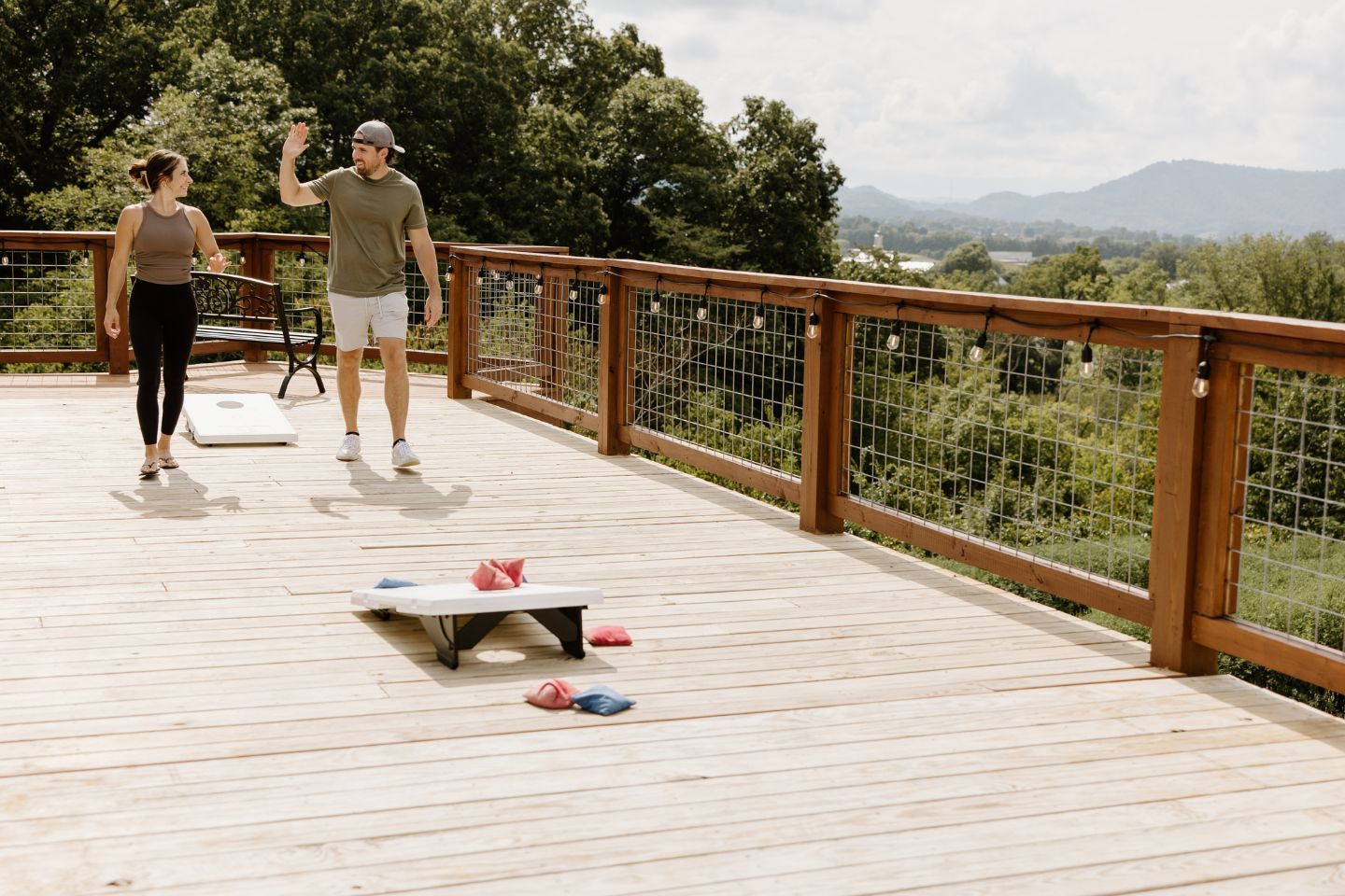 Couple playing cornhole on a deck at Sojourn Lodging with Smoky Mountain views in the background