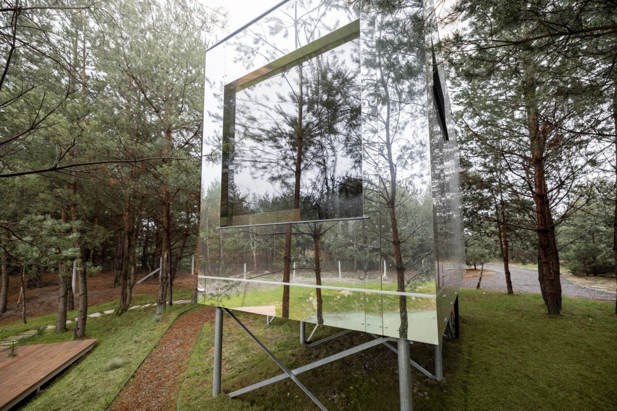 Mirror cabin set in between a forest and on legs.