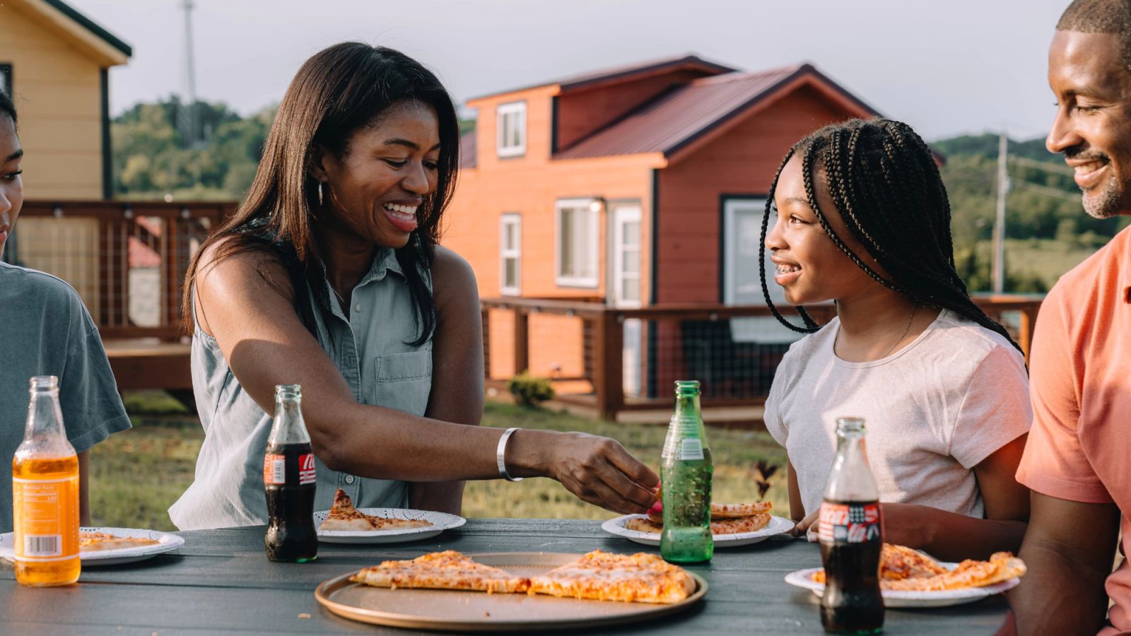 Friends sharing pizza and cold drinks around an outdoor table at Sojourn Lodging