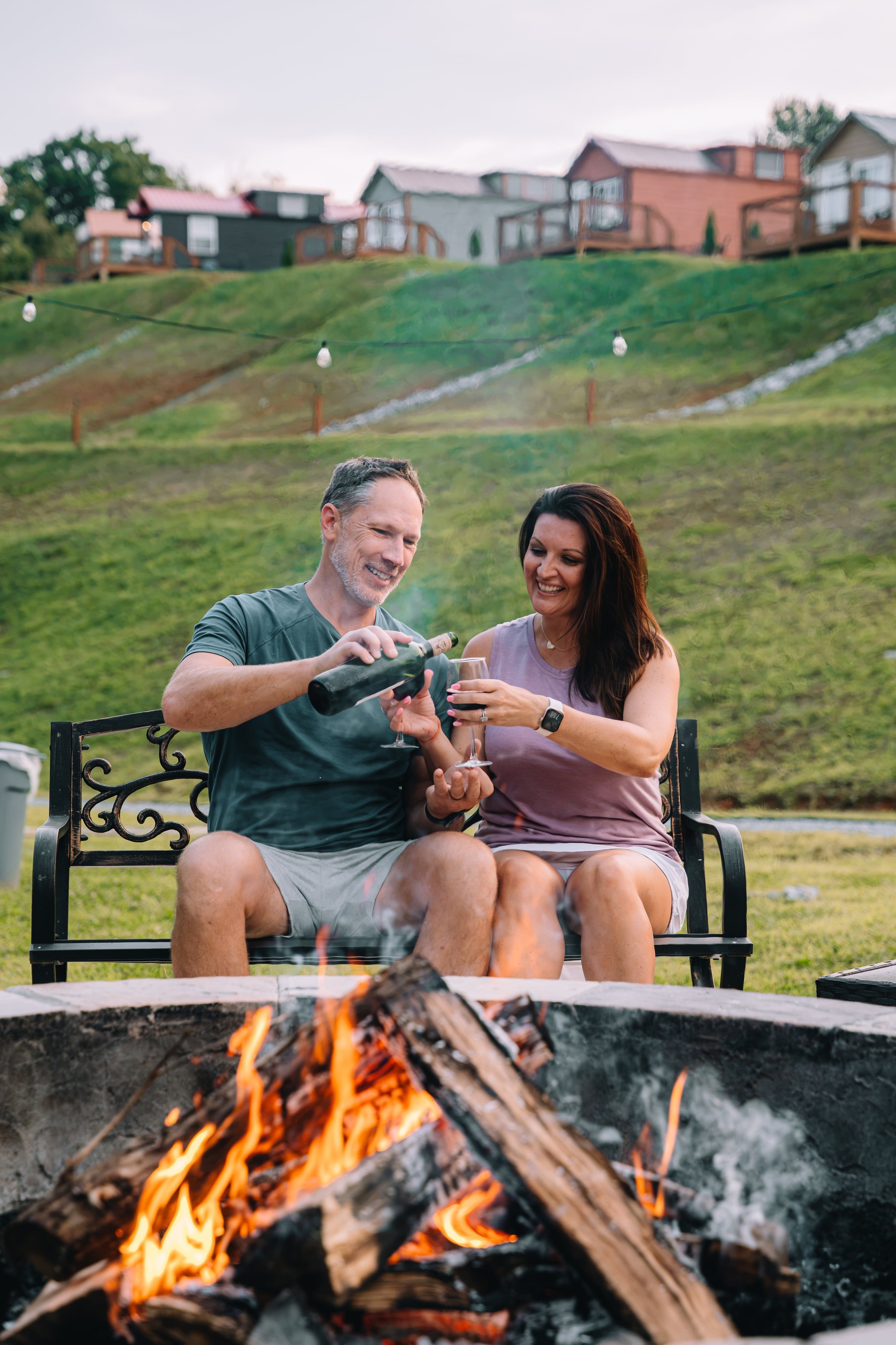 A couple toasting on the bench with the firepit burning in the foreground at Sojourn Lodging