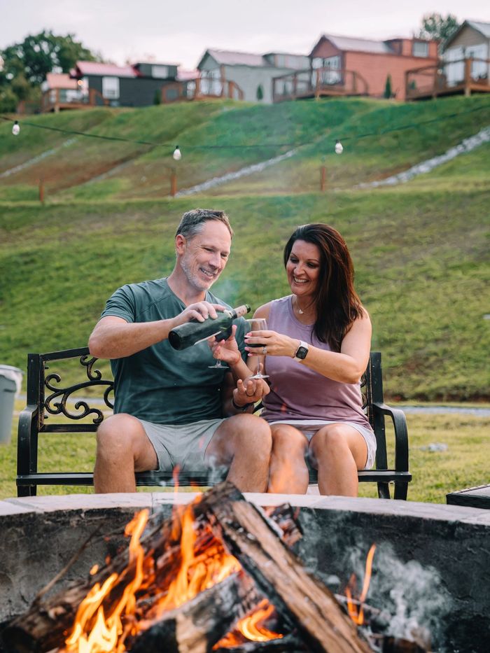 A couple toasting on the bench with the firepit burning in the foreground at Sojourn Lodging