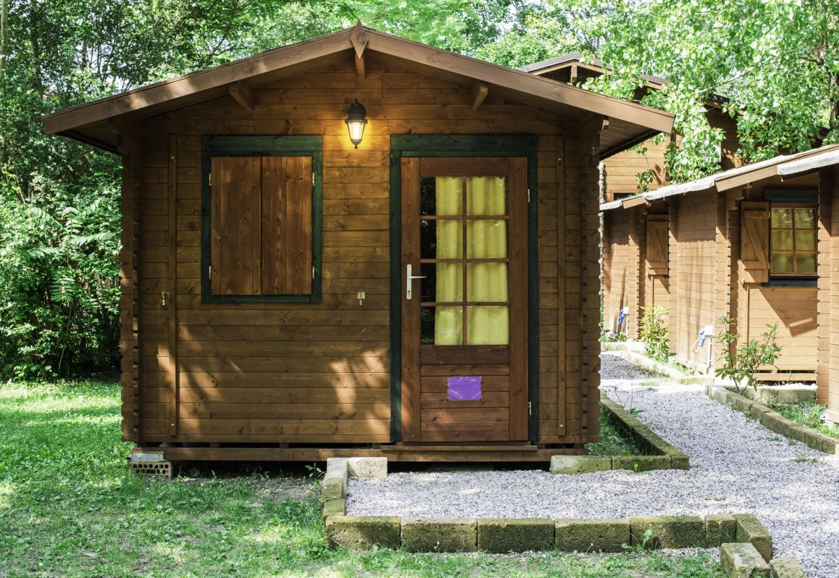 Wooden glamping bungalow with adjacent paved walkway.