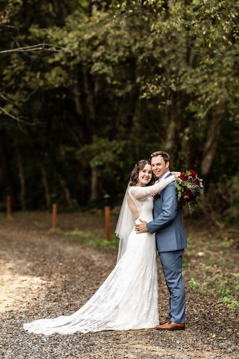 Bride and groom embracing on a gravel path surrounded by trees at Sojourn Lodging