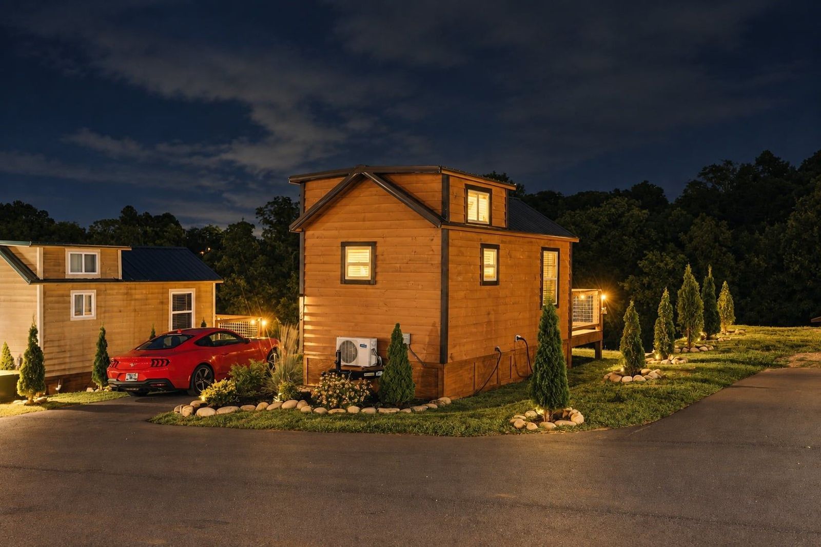 A cedar tiny home lit from within at night with a truck parked alongside at Sojourn Lodging