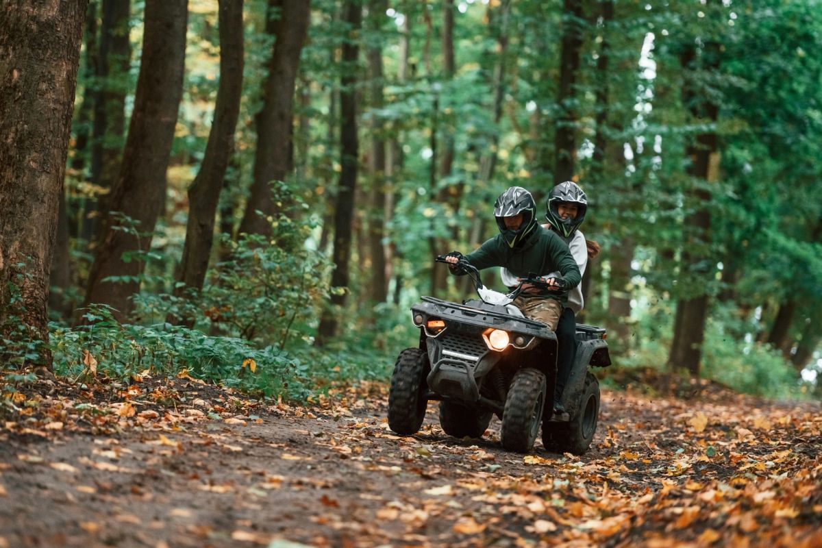 Two people riding through some trees on an ATV.