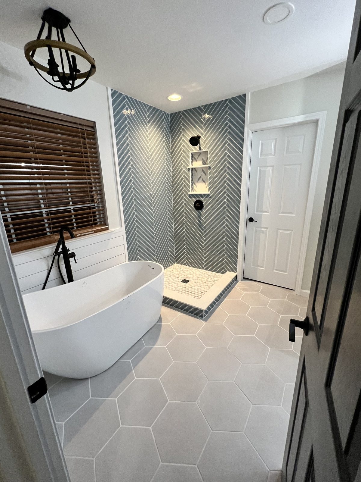 Freestanding soaking tub beside a blue herringbone tile shower