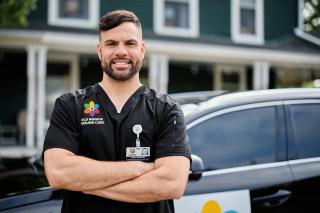 A mobile wound care nurse poses in front of a patient's home