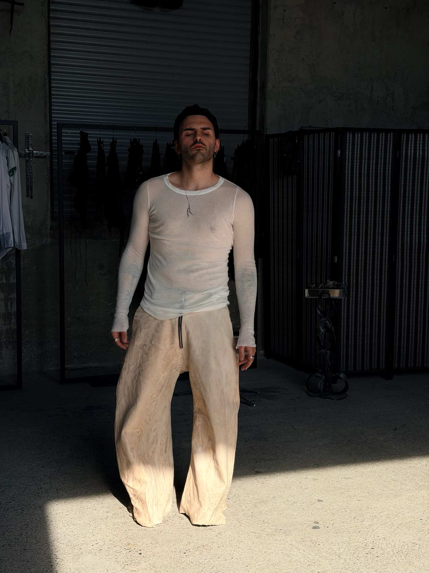 Uomo a figura intera con maglia trasparente e pantaloni chiari molto ampi.