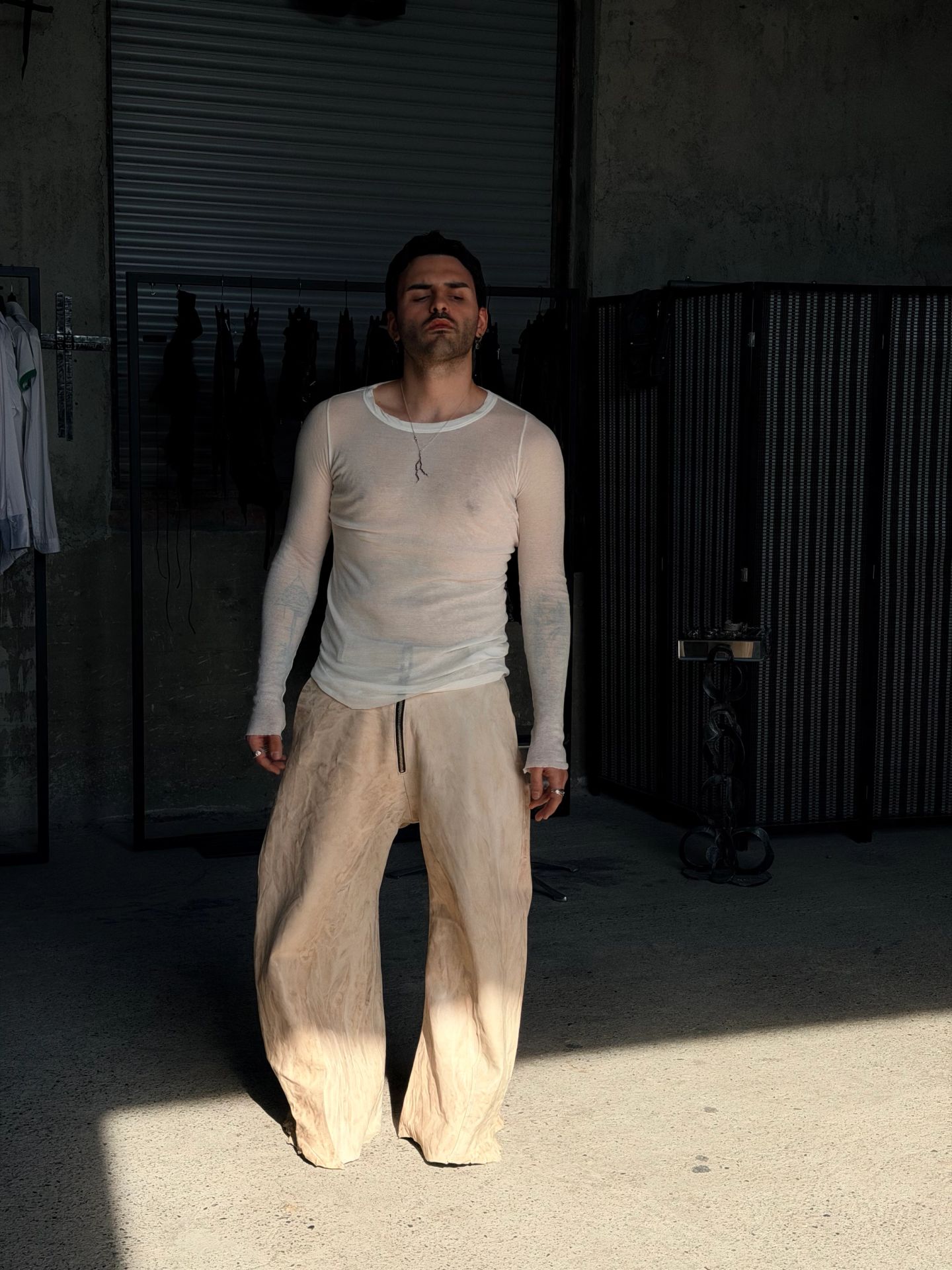 Uomo a figura intera con pantaloni chiari molto ampi, in laboratorio.